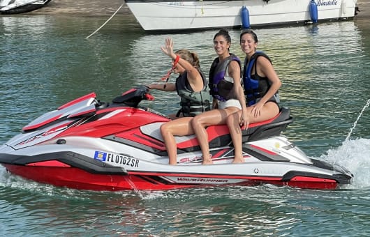 Three girls, all wearing life jackets, smiling while safely riding a jet-ski.