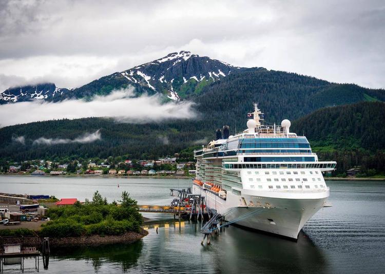 A large cruise ship at port in Alaska, with a tall snowy mountain in the background.